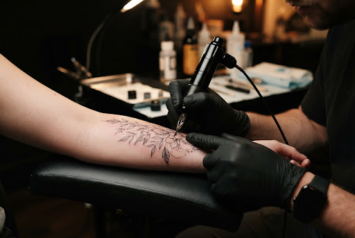 Fine line tattoo botánico en antebrazo con detalle de hojas y flores delicadas