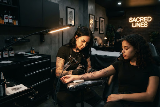Artista tatuadora trabajando concentrada con iluminación focalizada y máquina rotativa